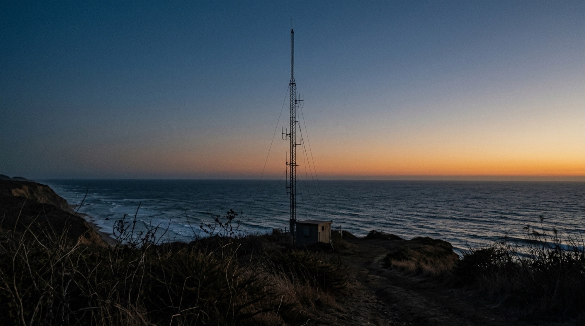 Radio antenna mast on a coastal bluff above the Pacific at dusk
